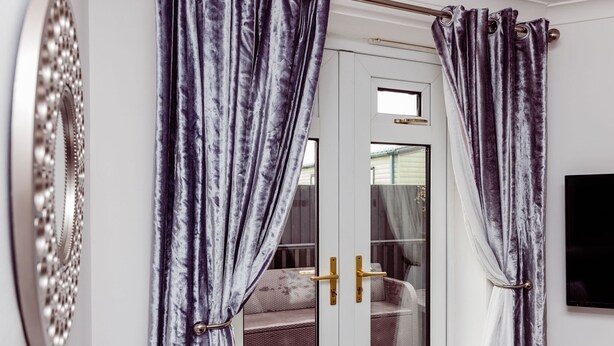A room with a sliding door, a sofa, and a television on the wall. - Willow Chalet (Grange-over-Sands)