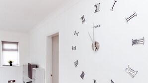 A room with a white wall clock made of nails and screws, a TV on a white stand, and a window with a plant. - Willow Chalet (Grange-over-Sands)