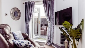 A living room with a leather sofa, a flat-screen TV, a large mirror, and a potted plant. - Willow Chalet (Grange-over-Sands)