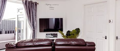 Una sala de estar con televisor, sofá y planta.