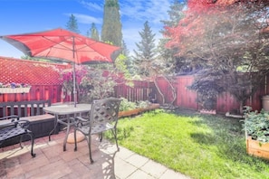 Relax in the serene patio surrounded by lush greenery and a vibrant red-leaved tree.