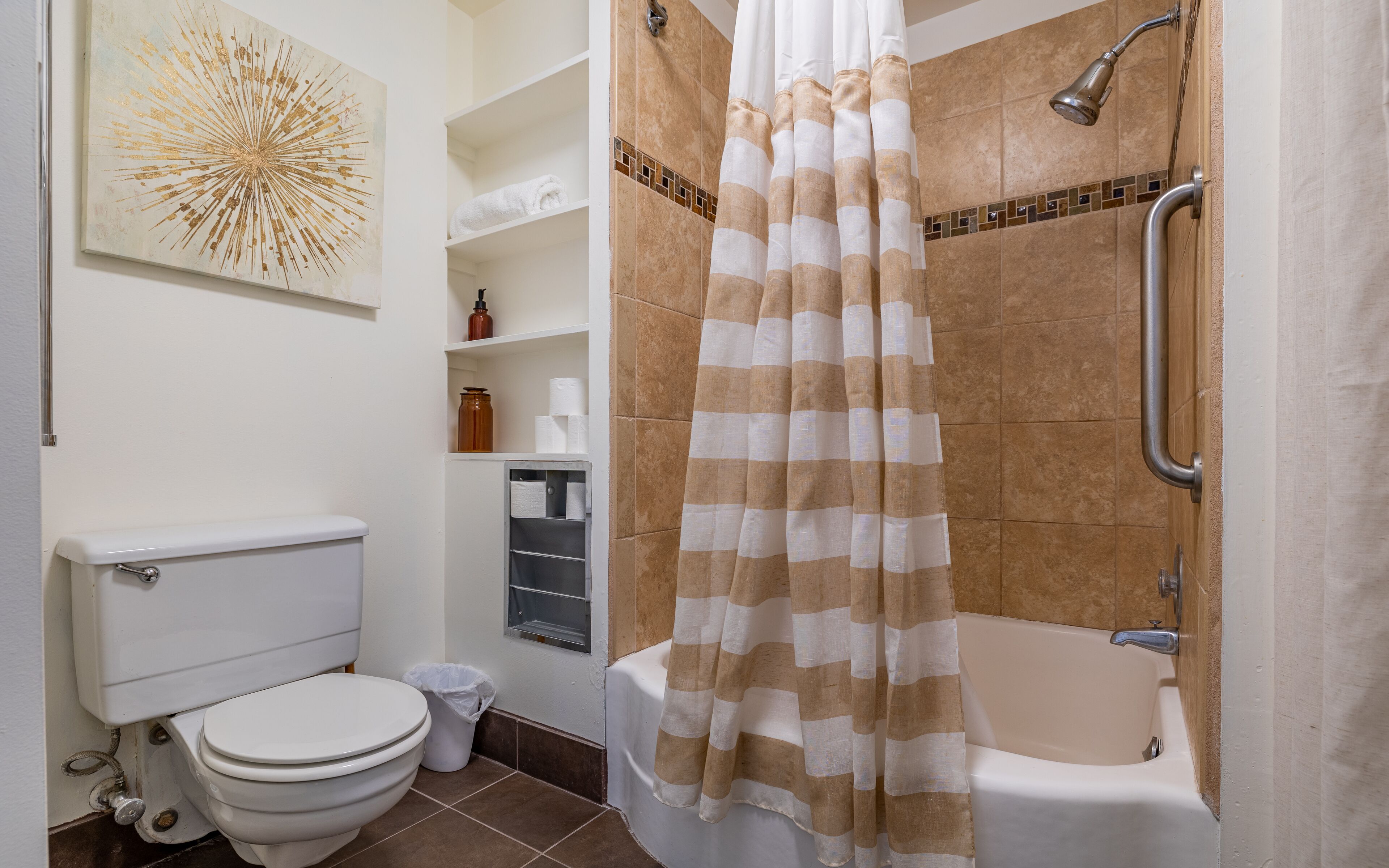 A bathroom with a toilet, a shower with a striped curtain, and a sink with a soap dispenser.