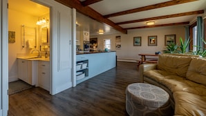 Eine geräumige Küche mit Holzbalken, ein Essbereich mit Tisch und Stühlen sowie ein Wohnzimmer mit Ledersofa und Hocker.