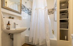 Ein Badezimmer mit weißem Waschbecken, einem Spiegel, einer Duschvorhang und einer Badewanne.