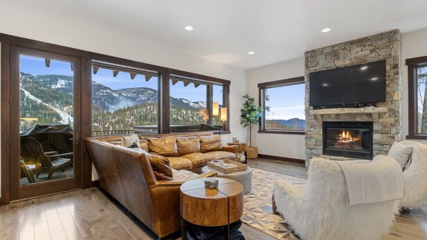 A spacious living room with a stone fireplace, a large flat-screen TV mounted above it, and a cozy seating area with a leather sofa and a fluffy armchair.