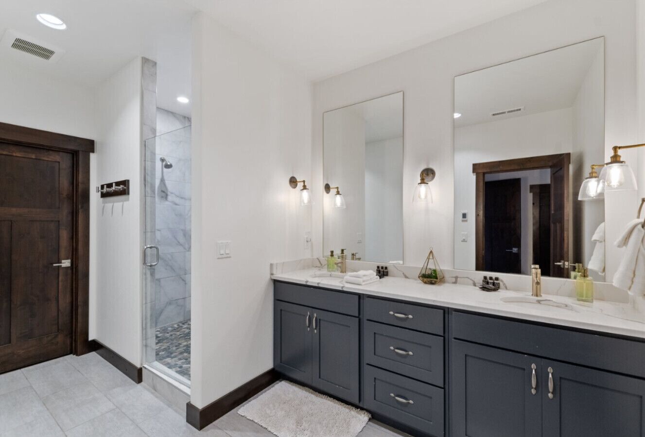 A modern bathroom with a walk-in shower, dark grey cabinets, and a large mirror.