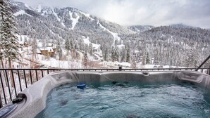 A hot tub with a view of snow-covered mountains and trees.