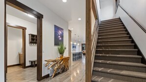 A modern interior with a wooden staircase, a dining area, and a hallway leading to a kitchen.