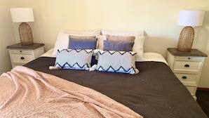 Un lit bien fait, recouvert d’une couvre-lit à motifs, agrémenté de deux coussins décoratifs, d’un plaid rose et de deux tables de chevet avec des lampes.