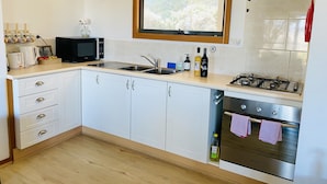 Une cuisine moderne avec des meubles blancs, un évier en acier inoxydable, un four à micro-ondes, une cuisinière à gaz et une fenêtre donnant sur un paysage verdoyant.