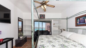 A bedroom with a bed, a ceiling fan, a TV, a window with a view, and a small table with a plant. - Marina Pinacate Remodeled 3 Bedroom 2 Bath Overlooking Sea of Cortez Views (Puerto Penasco)