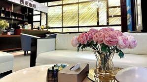A modern interior with a reception desk, a white sofa, and a vase of pink flowers. - Dong Do Minh Nguyet (Vo Cuong)