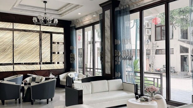 A modern hotel lobby with a white sofa, dark armchairs, and a large window offering a view of the street. - Dong Do Minh Nguyet (Vo Cuong)