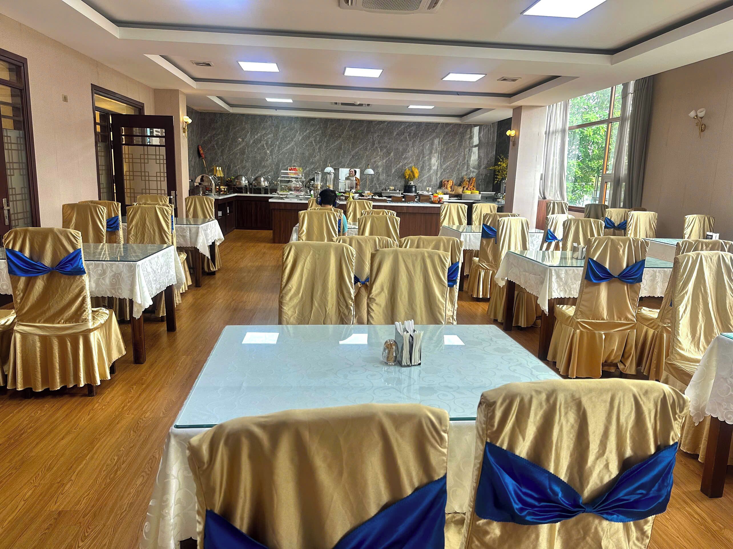 A banquet hall with tables covered in white tablecloths and chairs draped in gold fabric with blue sashes.