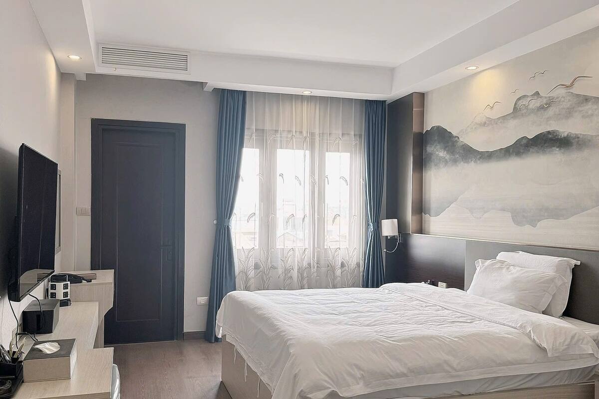 Ein modernes Hotelzimmer mit einem großen Bett, einem Schreibtisch und einem Flachbildfernseher, sowie einem Vogelgemälde an der Wand.