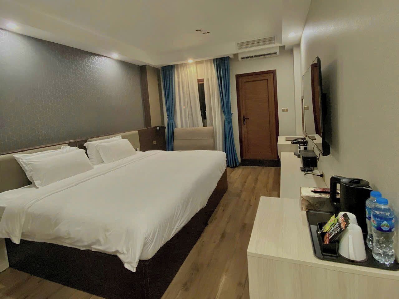 A hotel room with a large bed, a desk with a coffee maker, a water bottle, and a TV mounted on the wall.