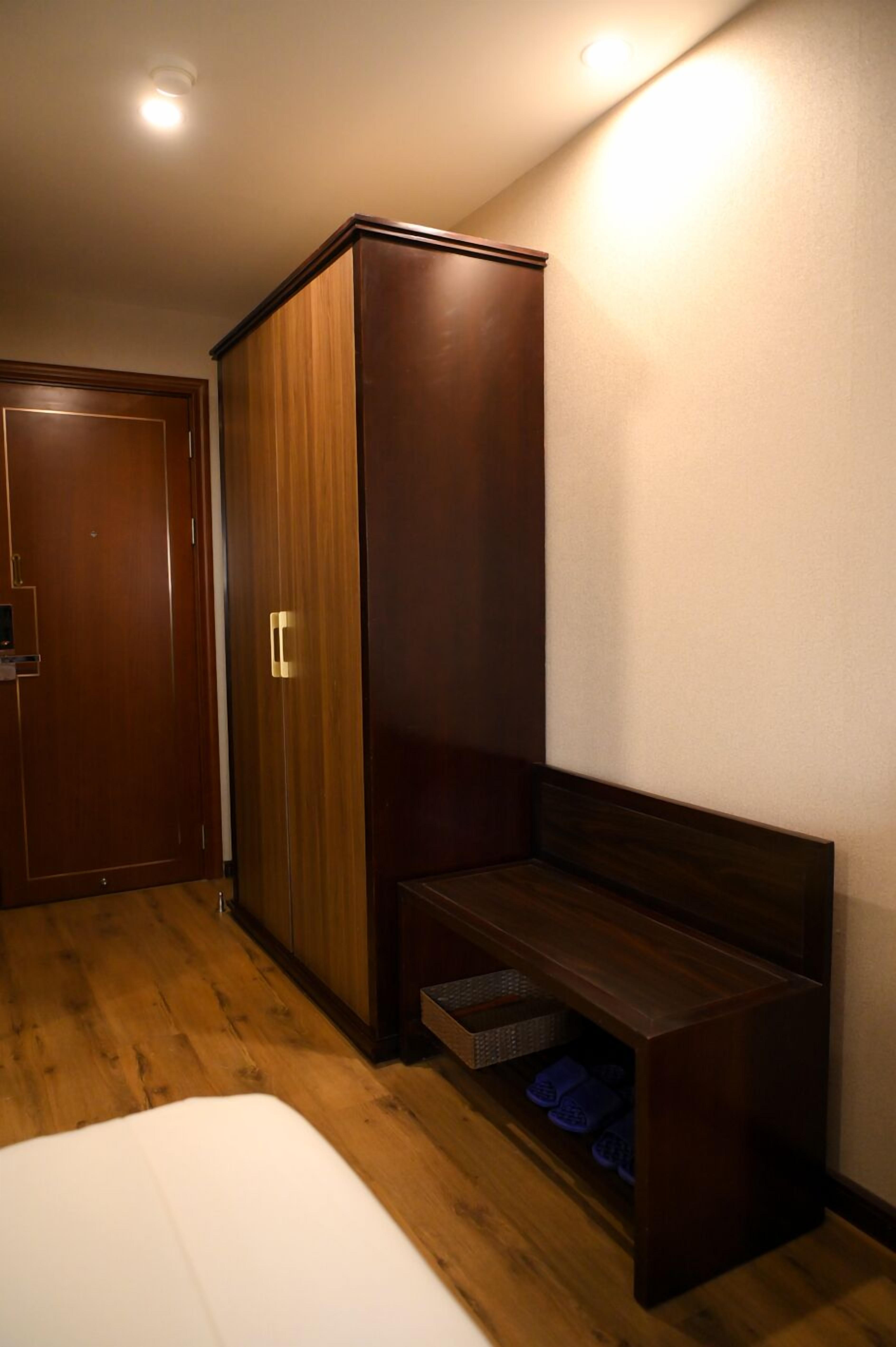 Un dormitorio con un armario de madera, un banco con zapatero y una puerta.