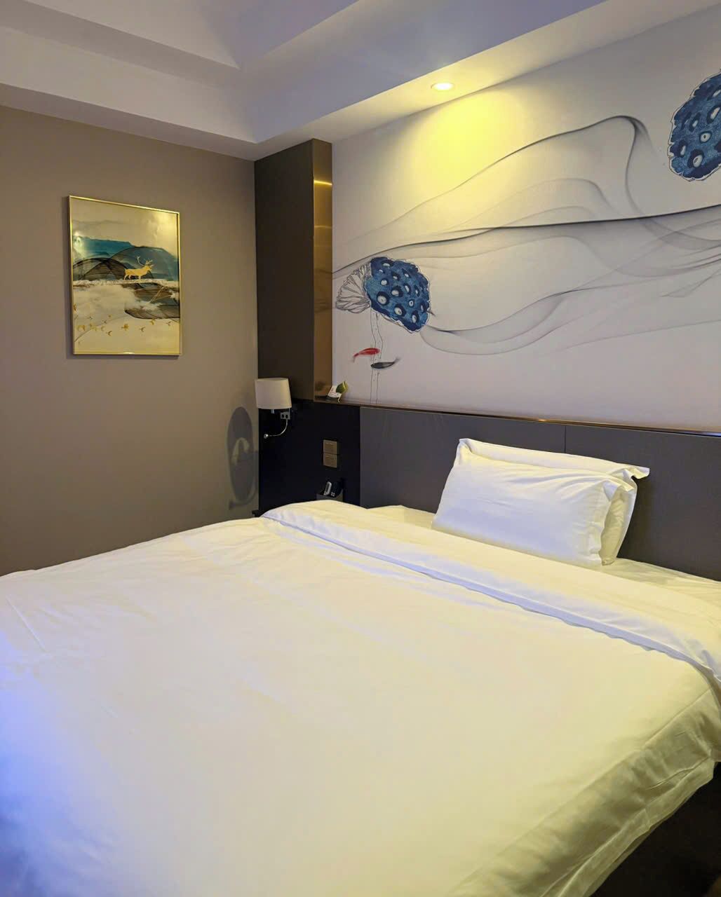 Una habitación de hotel con una cama grande, una obra de arte colgada en la pared y una mesita de noche con lámpara.