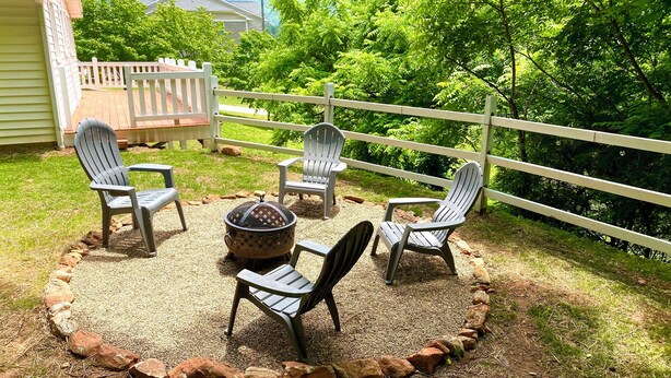 An outdoor seating area with Adirondack chairs and a fire pit, surrounded by a gravel path and a wooden fence. - Whisper Of Himalaya (Sylva)