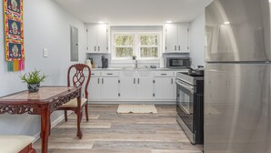 A modern kitchen with white cabinets, a stainless steel refrigerator, and a dining area with a wooden table and chairs. - Whisper Of Himalaya (Sylva)