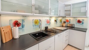 Eine moderne Küche mit einem schwarzen Spülbecken, weißen Schränken und einer Glasrückwand mit Obstmalereien.