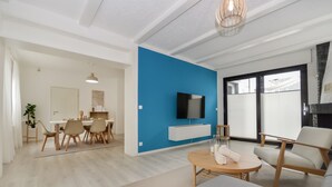 Ein modernes Wohnzimmer mit blauer Akzentwand, einem Flachbildfernseher und einem Essbereich mit Holzmöbeln.