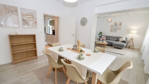 Ein moderner Essbereich mit einem weißen Tisch, beigen Stühlen und einem Holzregal.