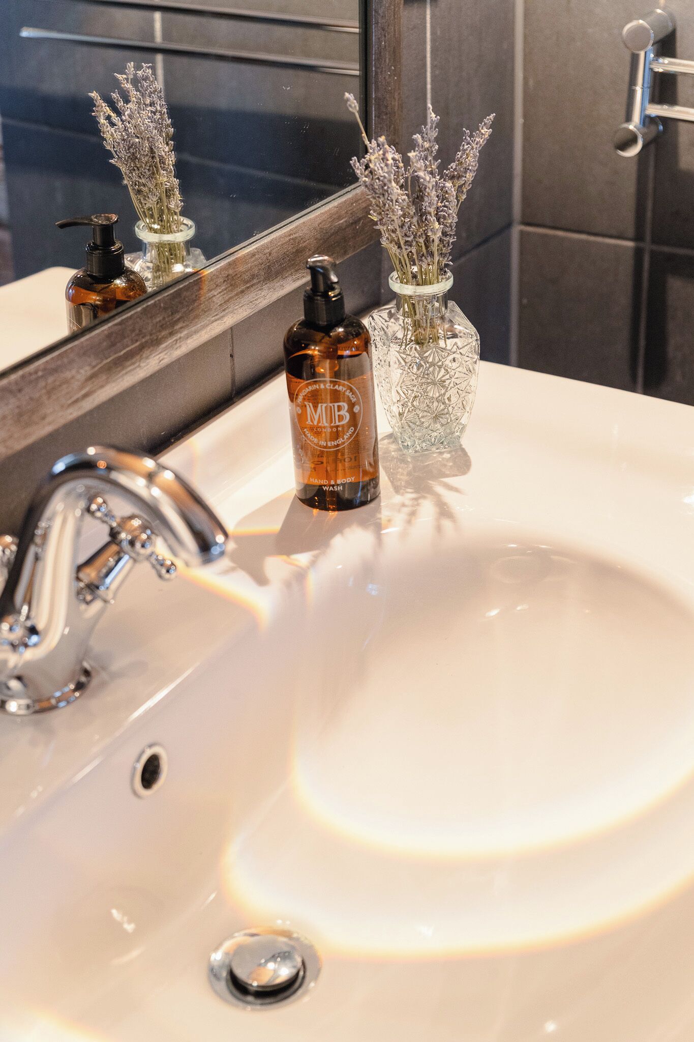 Een wastafel met spiegel, een lavendel vaas en een fles shampoo.