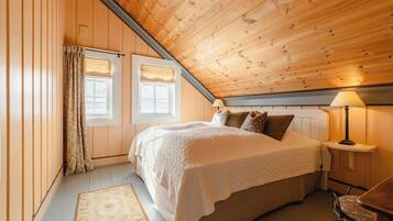 A bedroom with a wooden ceiling, a bed with a white bedspread, a nightstand with a lamp, and a window with curtains.