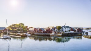Un pueblo costero con casas tradicionales rojas, una pequeña isla y barcos amarrados en el puerto.