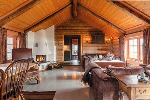 Interior d'una cabana de fusta amb una llar de foc, mobles de fusta i una zona d'estar acollidora.