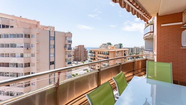 A balcony with a glass table and chairs, overlooking a cityscape with multiple buildings. - "El Toro" Apartment with Ocean View, Shared Pool, and Wi-Fi (Fuengirola)