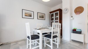 A dining area with a white table, four chairs, a clock, and two framed pictures on the wall. - "El Toro" Apartment with Ocean View, Shared Pool, and Wi-Fi (Fuengirola)