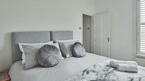 A bedroom with a bed, pillows, a blanket, and a window with blinds. - Hollie Cottage - Luxury Cottages (Lytham Saint Annes)