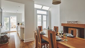 A dining area with a wooden table, chairs, and a fireplace. There is a window providing natural light and a view of the outside. - Hollie Cottage - Luxury Cottages (Lytham Saint Annes)