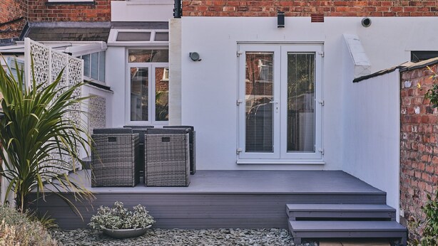 A modern house with a white exterior, a brick wall, and a small deck with outdoor furniture. - Hollie Cottage - Luxury Cottages (Lytham Saint Annes)