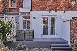 A modern house with a white exterior, a brick wall, and a small deck with outdoor furniture. - Hollie Cottage - Luxury Cottages (Lytham Saint Annes)