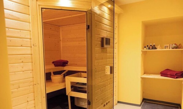 Un sauna en bois avec une porte en verre, une étagère avec des serviettes et une petite étagère avec des bouteilles.