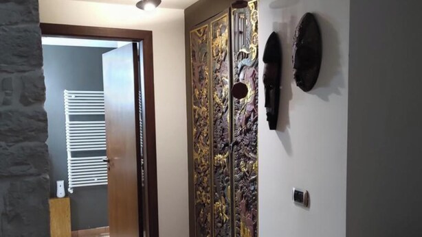 Un pasillo con suelo de baldosas, un panel decorativo en la pared, un ventilador de techo y un radiador.