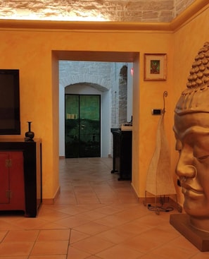 Un couloir avec une arche en pierre, une statue et un téléviseur posé sur un meuble.