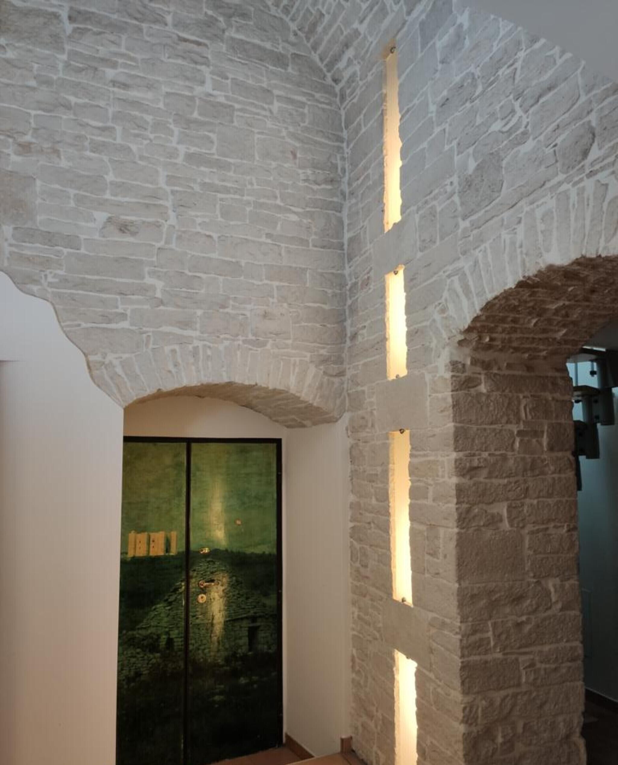 A room with stone walls, a large window, and a door with a green landscape view.