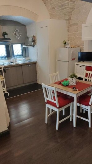 A dining area with a table and chairs, a kitchen with a refrigerator, and a stone wall. - Holiday Home 'L'orecchietta Studio' with Wi-Fi and Air Conditioning (Ruvo di Puglia)