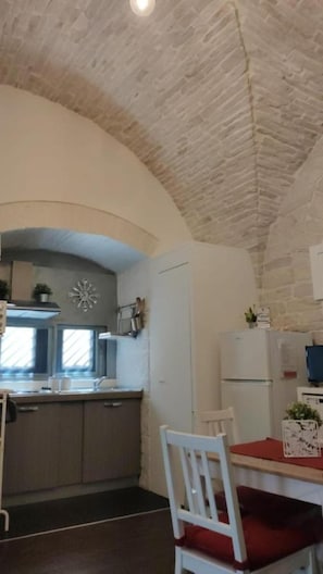 A kitchen with a stone ceiling, a dining area with a red table, and a white chair.