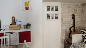 Een kamer met een stenen muur, een gitaar, een klein tafeltje met een mand en een rode stoel.