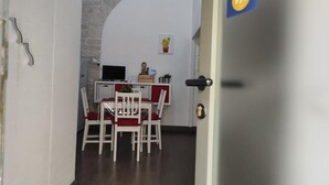 Een smalle gang die uitkomt in een eetruimte met een witte tafel en stoelen, een televisie en een stenen muur.