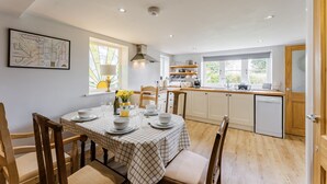 A dining area with a table set for four, a kitchen with white cabinets, and a map on the wall. - Bar Lane Cottage - sleeps 5 in Reepham (Reepham)