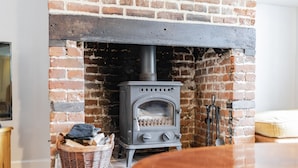 A brick fireplace with a wood-burning stove, a wicker basket, and a wooden table. - Bar Lane Cottage - sleeps 5 in Reepham (Reepham)