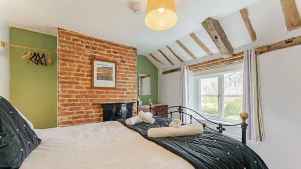 A bedroom with a brick wall, a bed with black and white bedding, a window with curtains, and a hanging light fixture. - Bar Lane Cottage - sleeps 5 in Reepham (Reepham)