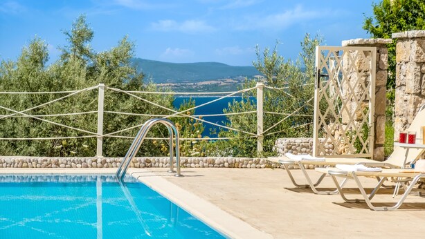A pool with a view of the sea, surrounded by lounge chairs and a stone wall. - Apartment 'Oceanida Aelia Room 2' with Shared Pool and Wi-Fi (Nikiana)