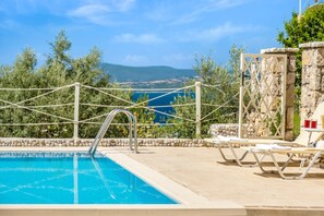 Una piscina con vista sul mare, circondata da lettini e un muro in pietra.